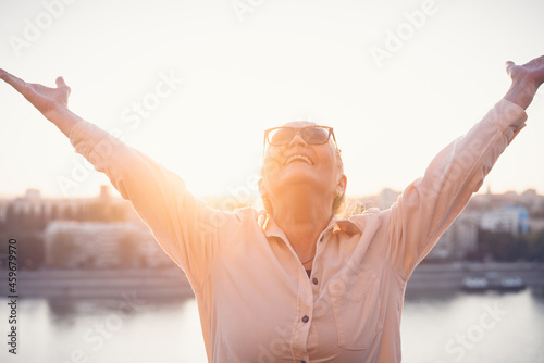 Portrait of happy attractive expressive exited mature senior woman 60 years old with hands up at sunset
