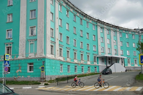  Russia, Murmansk region. Kirovsk. On a cloudy summer day, two teenage boys ride bicycles through a pedestrian crossing near the building of the hotel 