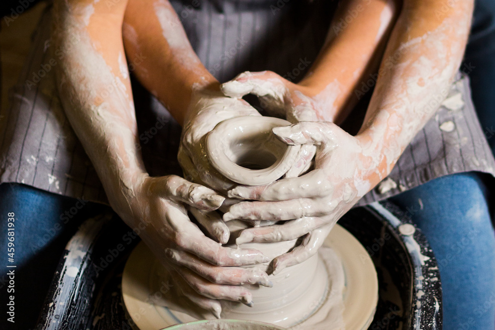 Pottery making. Smeared in clay hands of man and woman on potter's wheel. A couple is making a vessel or a bowl or a vase