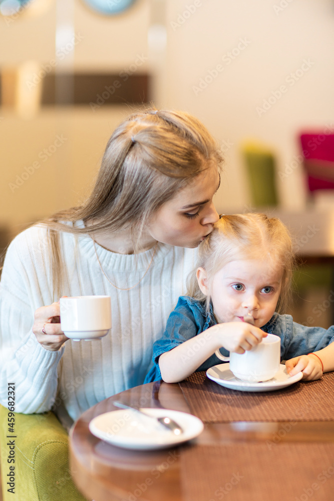 Mom kisses the baby. Mom and daughter eat in a cafe. Mom kisses the baby. Mom and daughter eat in a cafe.