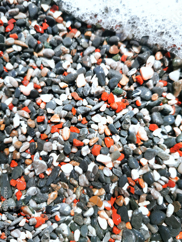 A sea beach with small colored pebbles and foam