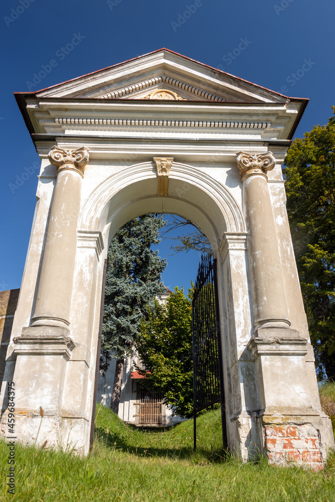 Fototapeta premium Classicist gate at the entrance to a country cemetery with a baroque chapel