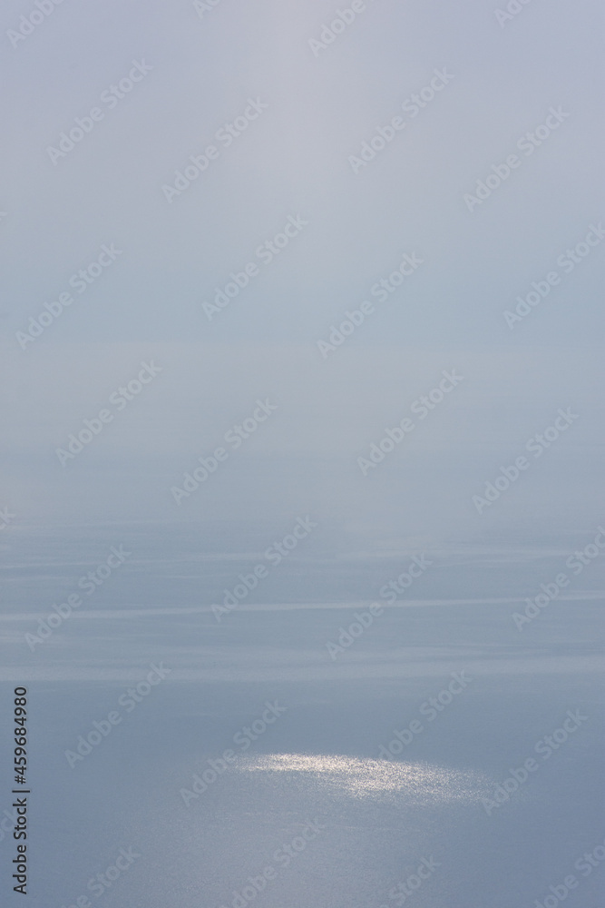 Sea ray Sea ray minimalism. A vertical atmospheric empty landscape with fog over the water and one penetrating ray of sun. Natural air background, mockup for marine design of postcards, brochures, ban