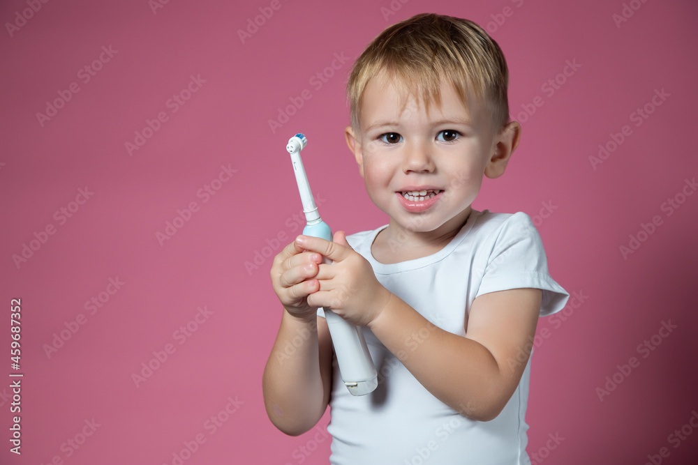Smiling caucasian little boy holds electric sonic toothbrush on pink background Smiling caucasian little boy holds electric sonic toothbrush on pink background