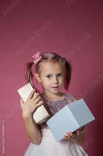 Little caucasian girl in a festive dress with sequins posing opening gift box