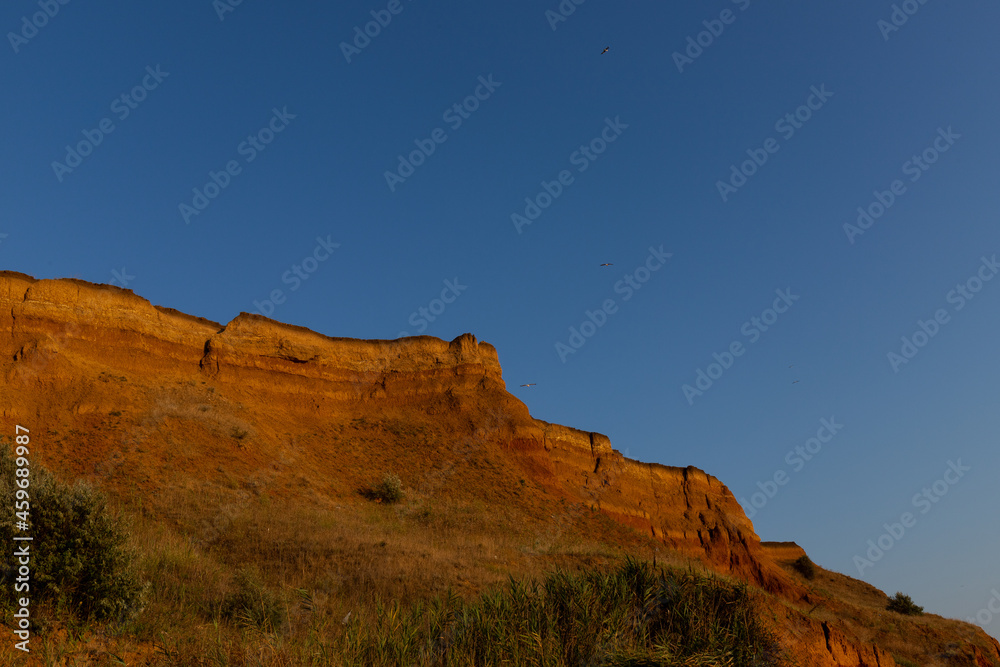 Fototapeta premium Geology. Desert landscape. Panorama view of the sandstone formation, the rocky cliffs, sand. Background or texture of sandy cliff on the coast, orange limestone