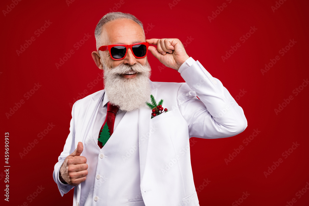 Photo of positive happy charming old man look empty space wear sunglass xmas isolated on red color background Photo of positive happy charming old man look empty space wear sunglass xmas isolated on red color background