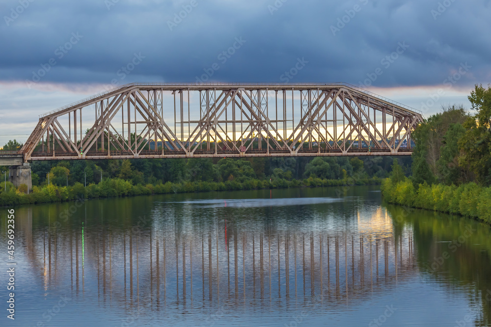 Railway transport bridge made of steel piles and beams across the river during sunset