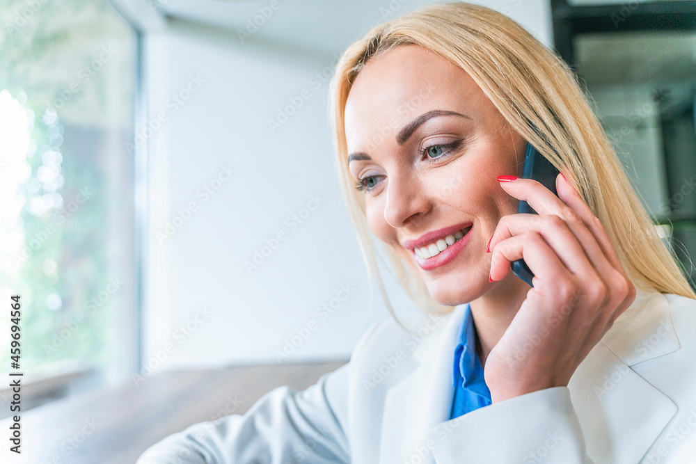 Smiling blond businesswoman talking on smart phone in office Smiling blond businesswoman talking on smart phone in office