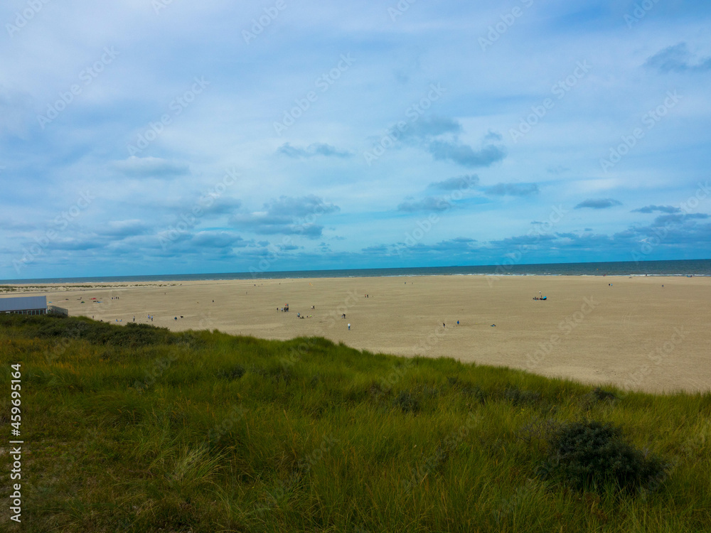 Panorama view of Dunes with marram grass and an empty beach on the Dutch island of Texel on a  with a blue cloudy sky in summer. National park Duinen van Texel  Tourism and vacations concept.	