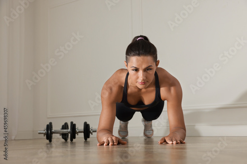 Young woman doing plank exercise on floor indoors
