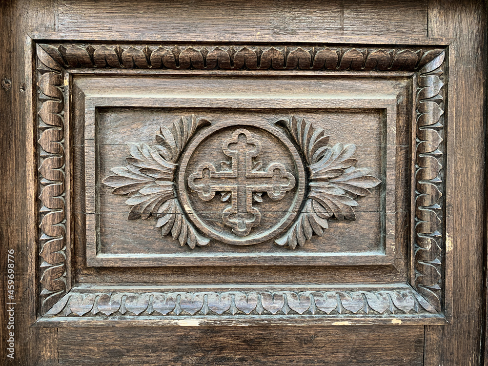 Engraved cross symbol with ornaments on old wooden door of a christian church.