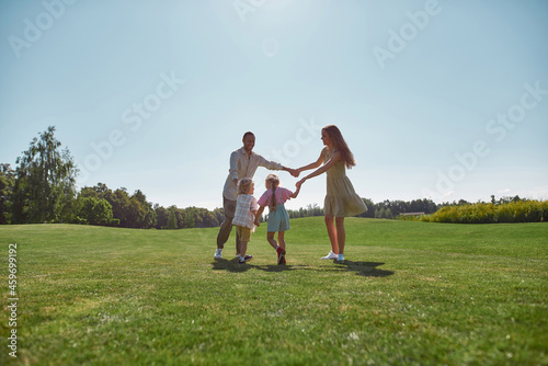 Happy family enjoying leisure activity, spending time together with two little kids, boy and girl in green park on a summer day