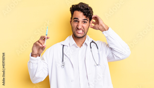 hispanic handsome man feeling stressed, anxious or scared, with hands on head physician and srynge concept photo