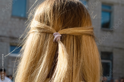 close-up - a girl with long blond loose hair, two strands of hair are gathered with an elastic band for hair in a bun