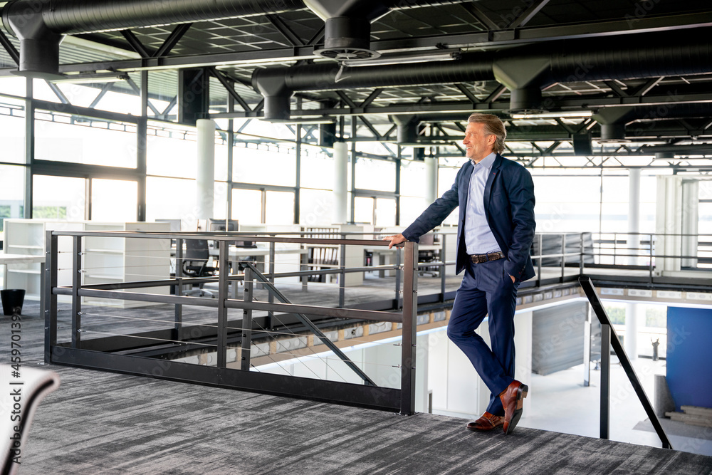 Businessman with hand in pocket standing by railing in office