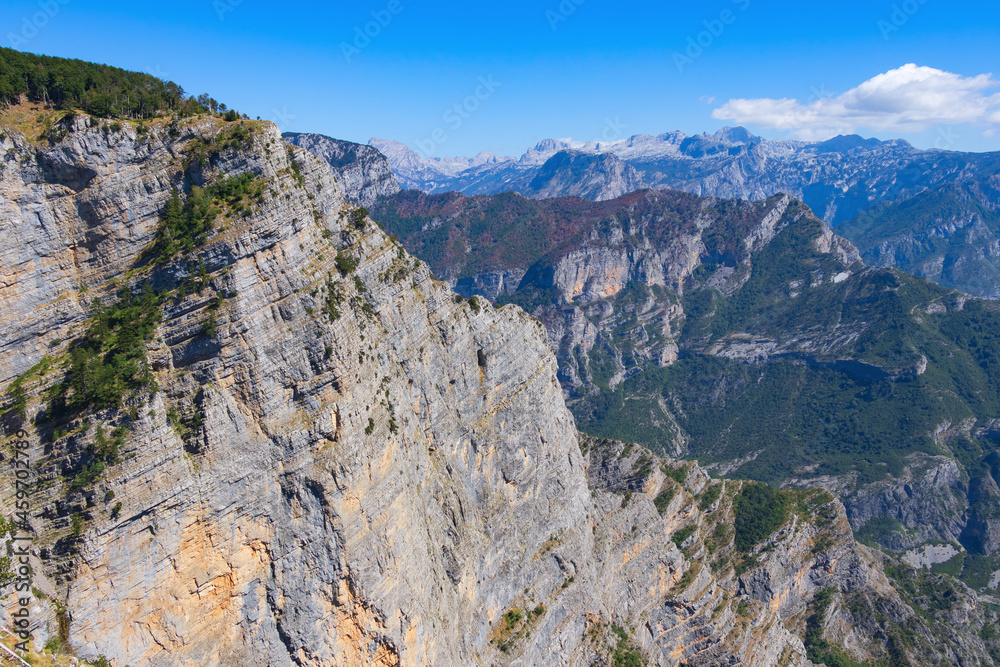 Breathtaking panoramic view of the Grlo Sokolovo gorge in Montenegro. In the foreground is a mountain, the flat side of which forms a cliff, and the ridge is overgrown with trees
