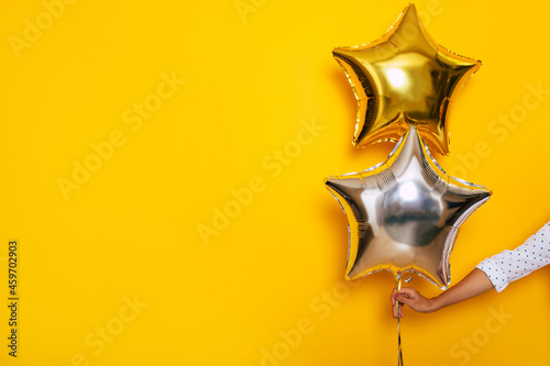 Young female hand holds a bright balloon in the shape of a star on the yellow background