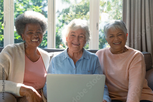 Three happy diverse senior woman sitting on sofa and using laptop
