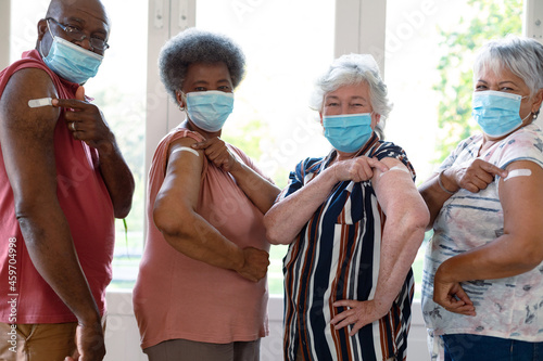 Four diverse male and female senior friends wearing face masks showing plasters after vaccination