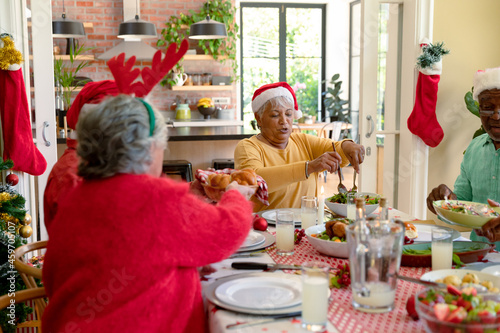 Diverse group of happy senior friends in holiday hats celebrating christmas together at home