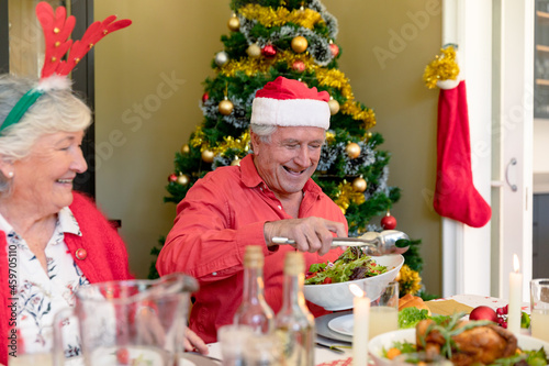 Happy caucasian senior couple in holiday hats sitting at christmas table