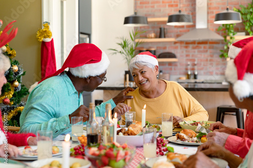 Diverse group of happy senior friends in holiday hats celebrating christmas together at home