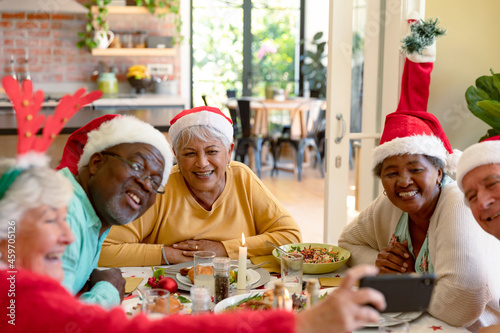 Diverse group of happy senior friends in holiday hats celebrating christmas together  taking selfie