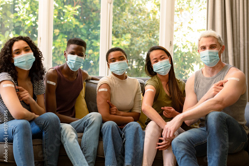 Group of happy diverse female and male friends in face masks showing plasters after vaccination