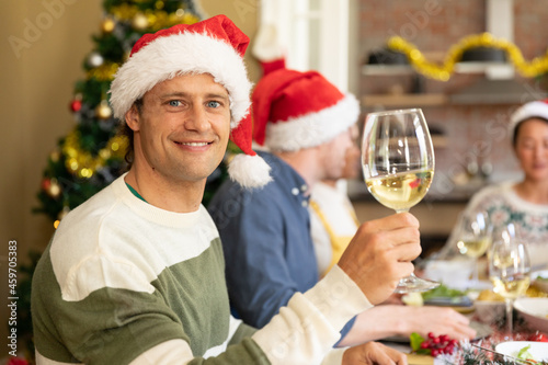 Happy caucasian man in santa hat toasting, celebrating christmas with friends at home