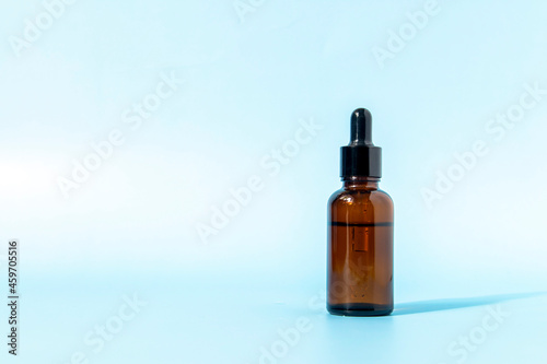 Glass dropper bottle made of brown glass on a blue background casts a shadow. Front view with copy space. Mockup of a cosmetic product. Serum for skin care.