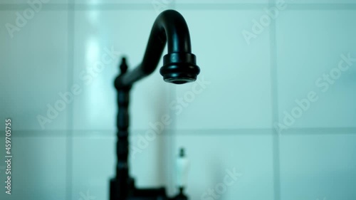 close-up of stream of water flowing, female hand opens black water tap in kitchen in retro style, blurred background, green backlighting, selective focus, concept of saving water resources, thirst photo