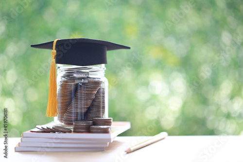 Graduation hat on coins money in the glass bottle on natural green background, Saving money for education concept photo