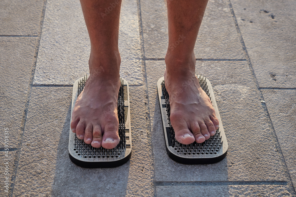 Male feet stand on a board with sharp nails. Sadhu's board. Practice yoga at dawn in the morning sun. Pain, trials, health, relaxation, cognition. Close-up Male feet stand on a board with sharp nails. Sadhu's board. Practice yoga at dawn in the morning sun. Pain, trials, health, relaxation, cognition. Close-up