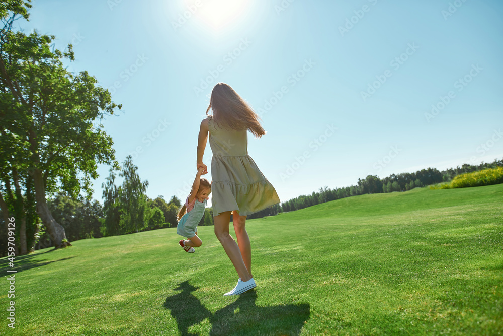 Full length shot of mom and little daughter spending time together on grass field in summer park Full length shot of mom and little daughter spending time together on grass field in summer park