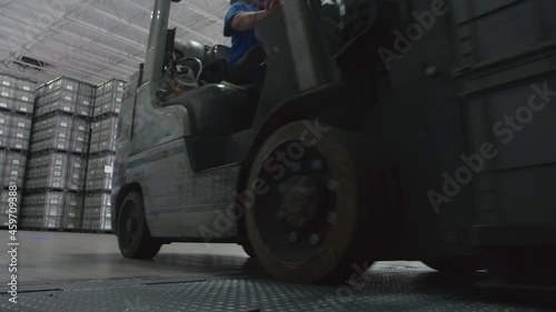 Forklift with Heavy Load Drives onto Ramp Past Camera In Manufacturing Warehouse