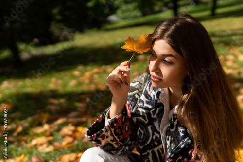 Autumn portrait of a beautiful girl with a maple leaf in her hand