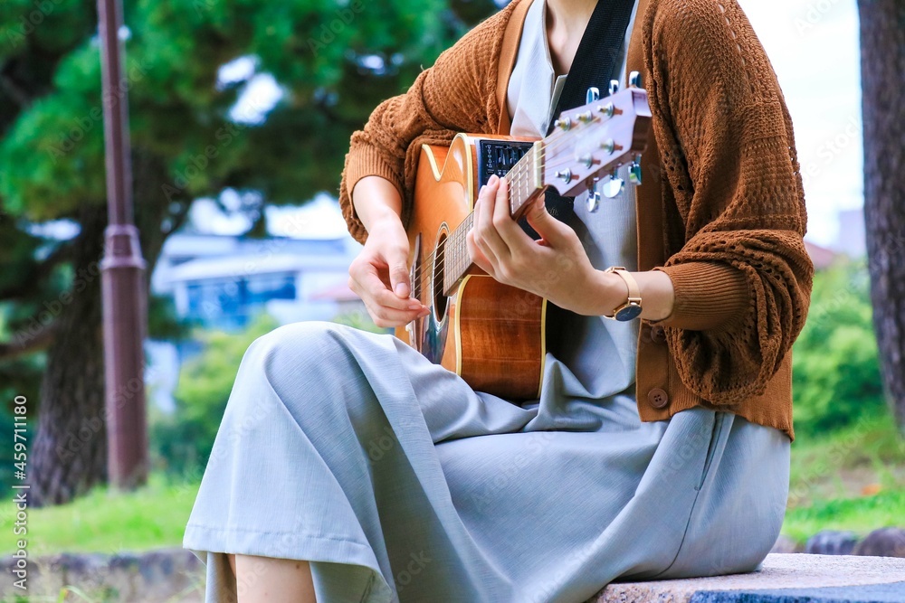 公園のベンチでアコースティックギターを弾く女性