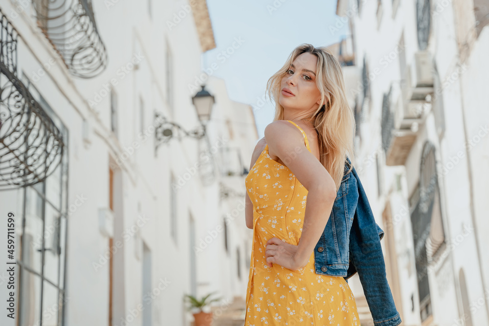 Stylish woman in bright dress and denim jacket standing in old city Stylish woman in bright dress and denim jacket standing in old city