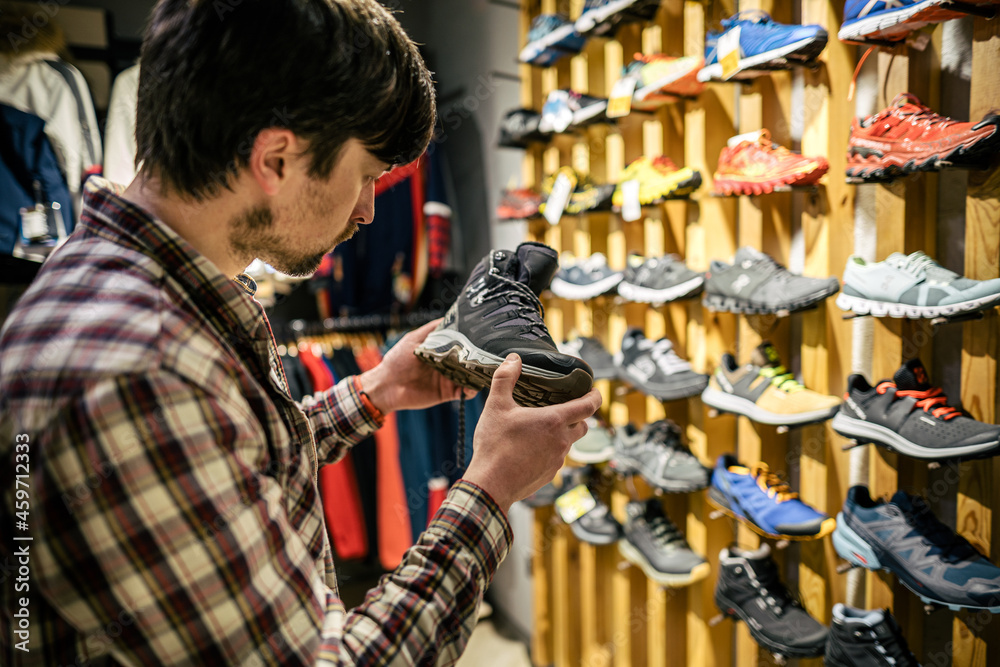 Man shopping in an outdoor store. Male buying mountain boots. Shopper in sports store select hiking shoes. Customer purchase of footwear for adventures. Man trying mountaineering boots at travel shop