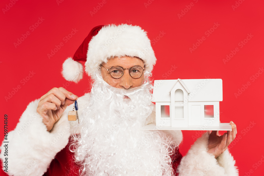 Santa claus in costume holding key and house model isolated on red