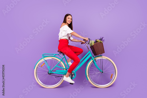 Photo of cheerful lady ride bicycle spring weekend wear white blouse trousers shoes isolated purple color background © deagreez