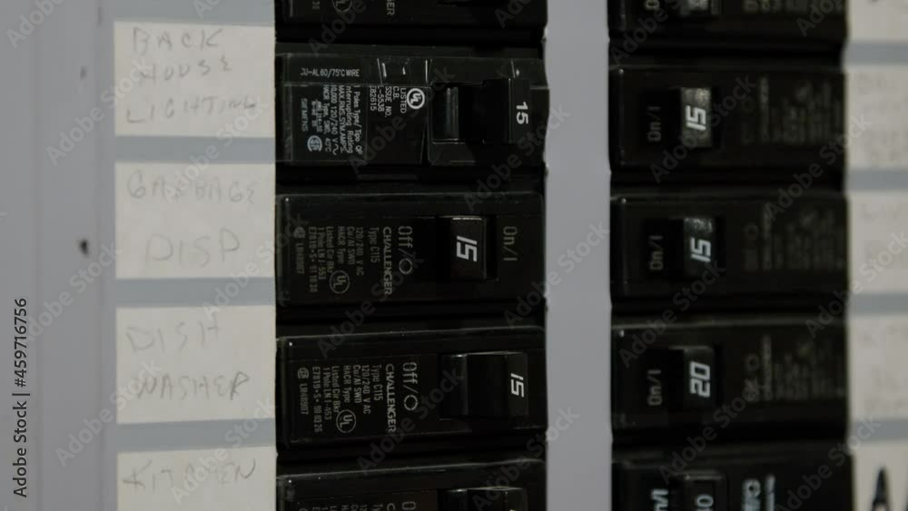 Male electrician turning off power for electrical outlet at circuit breaker box. Resetting Tripped breaker