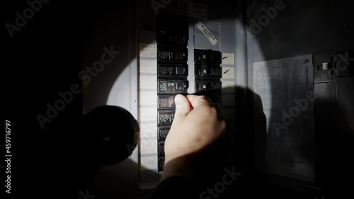 Man uses Flashlight At Breaker Fuse Box During Power Electricity Outage storm