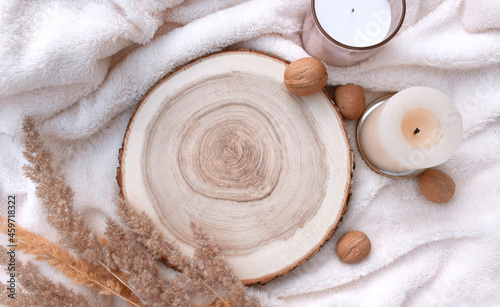 Cozy winter mockup still life scene with wooden round tray, candles and walnuts on white plaid. Nordic home decor flat lay for Christmas holidays or Thanksgiving. Trendy eco layout concept.