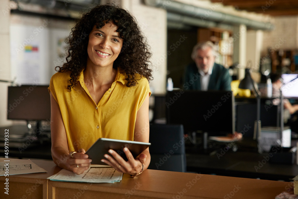 Smiling businesswoman with digital tablet leaning on table in office Smiling businesswoman with digital tablet leaning on table in office