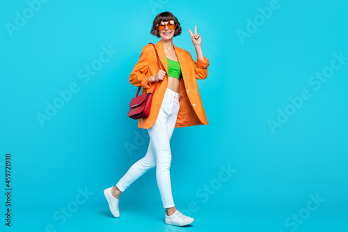 Full length profile photo of sweet millennial brunette lady go wear blazer spectacles top jeans shoes isolated on teal background