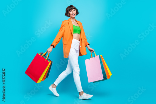Full length photo of happy woman hold hands shopping bags walk smile isolated on pastel blue color background
