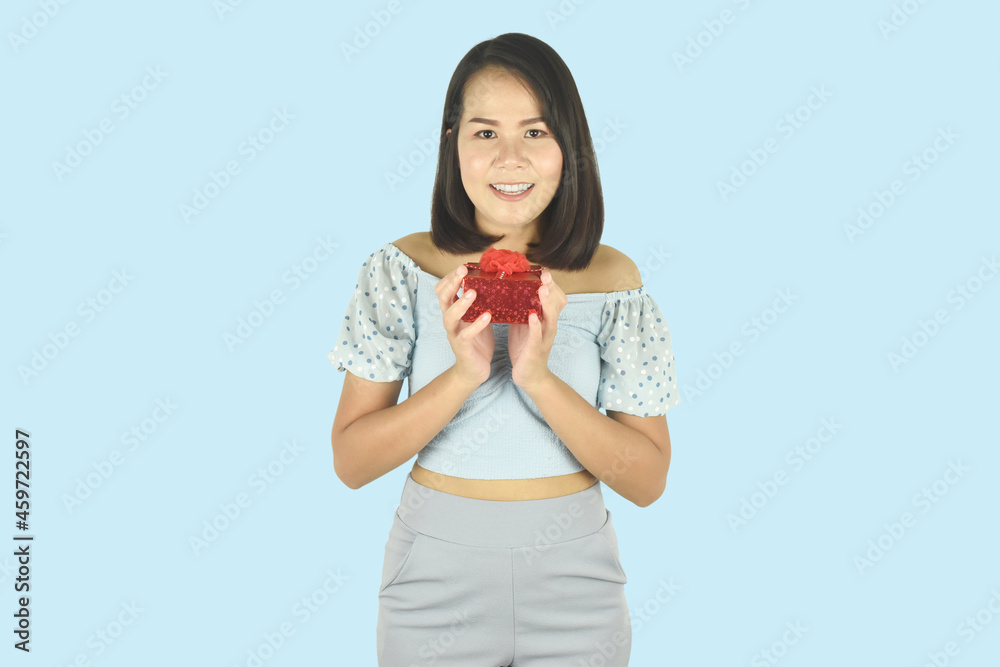 Portrait of young woman holding red gift box with red ribbon and showing happy gesture on blue background. Portrait of young woman holding red gift box with red ribbon and showing happy gesture on blue background.