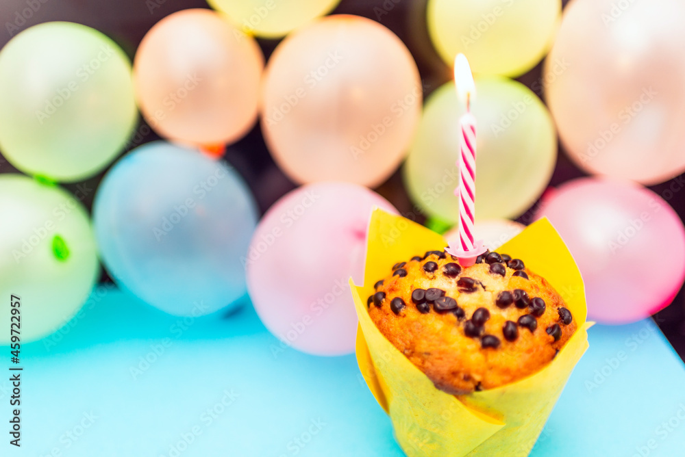 Birthday cupcake.Pastel yellow birthday cupcake with candle and blurred balloons.colorful birthday.Closeup,copy space.